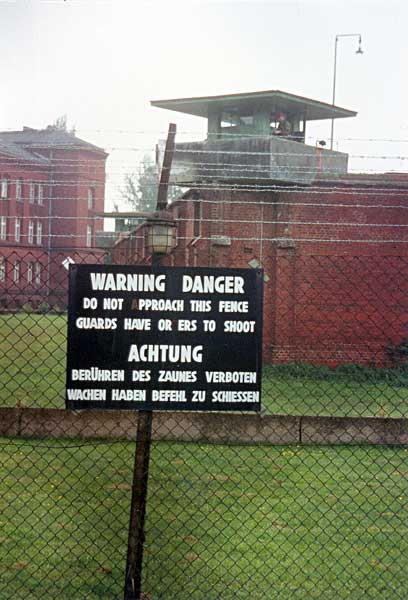 Сторожевая вышка на тюремной стене и предупредительная надпись на двух языках